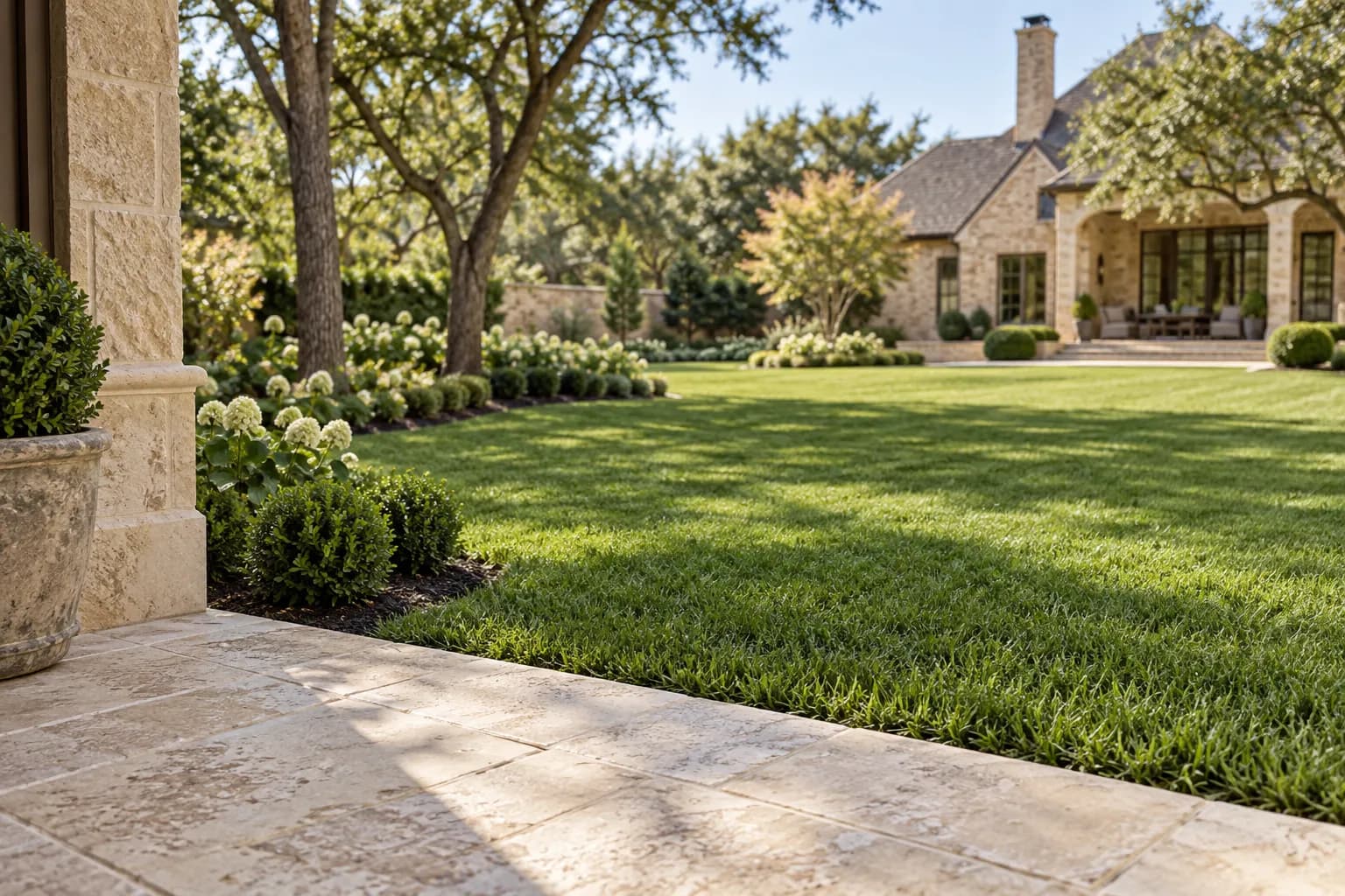 A limestone patio meeting an open lawn and neatly maintained garden beds